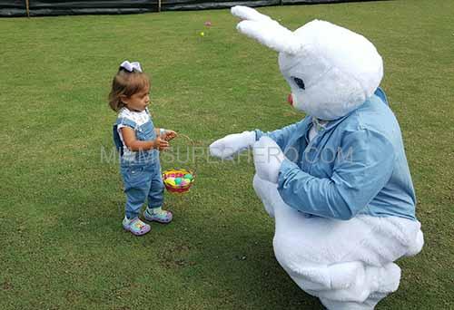 Alt: Easter Bunny helping toddler collect eggs during Easter egg hunt party event