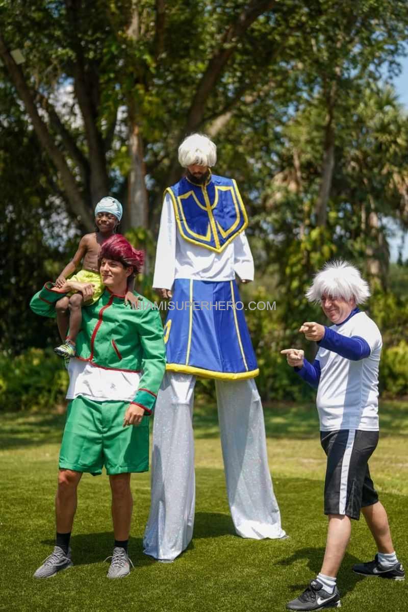 Killua pointing beside Gon and stilt-walking Kurapika with a young guest