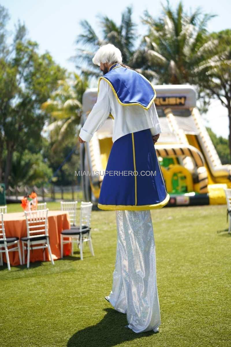 Stilt-walking Kurapika crossing the party lawn past the bounce house